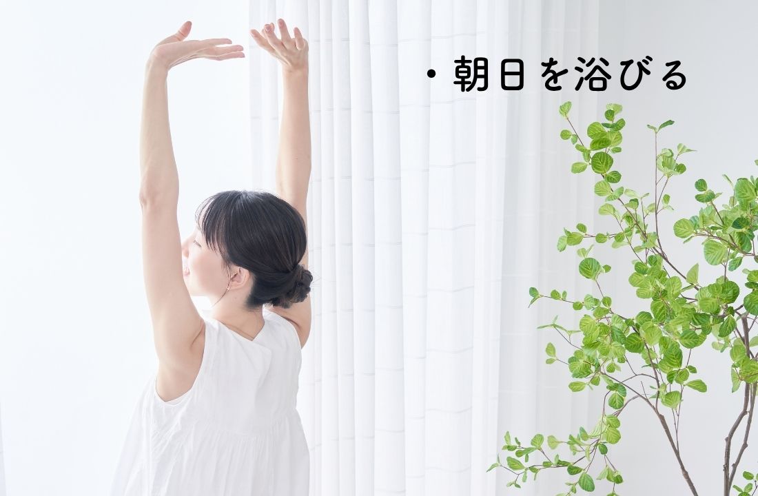 朝日をカーテンの前で浴びる女性